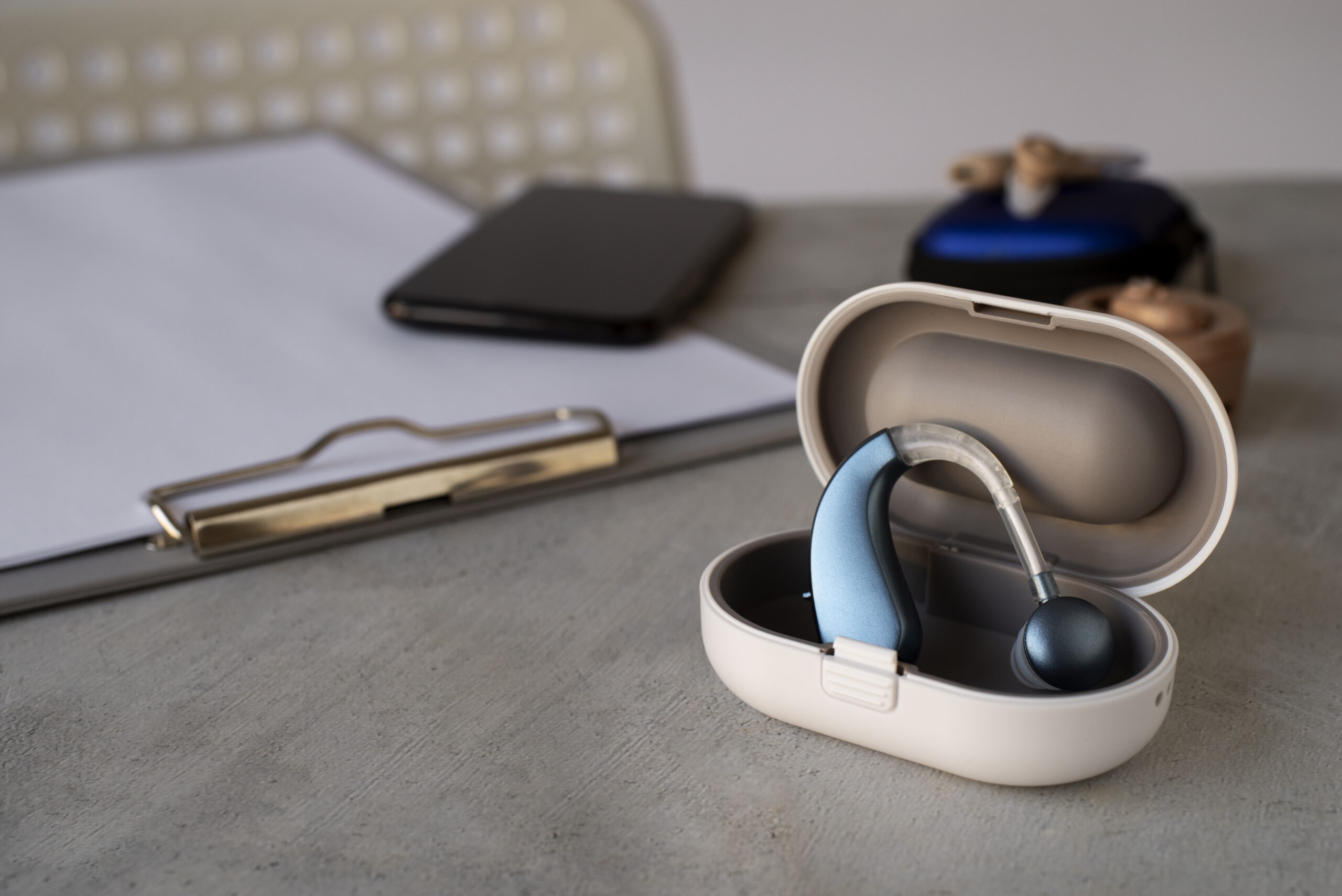 Hearing aid in a charging case on a desk in a professional workspace.