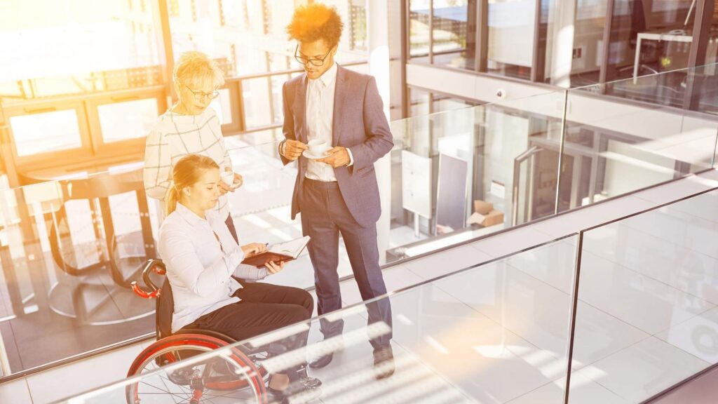 Professionals discussing work in a modern office environment, including a wheelchair user.
