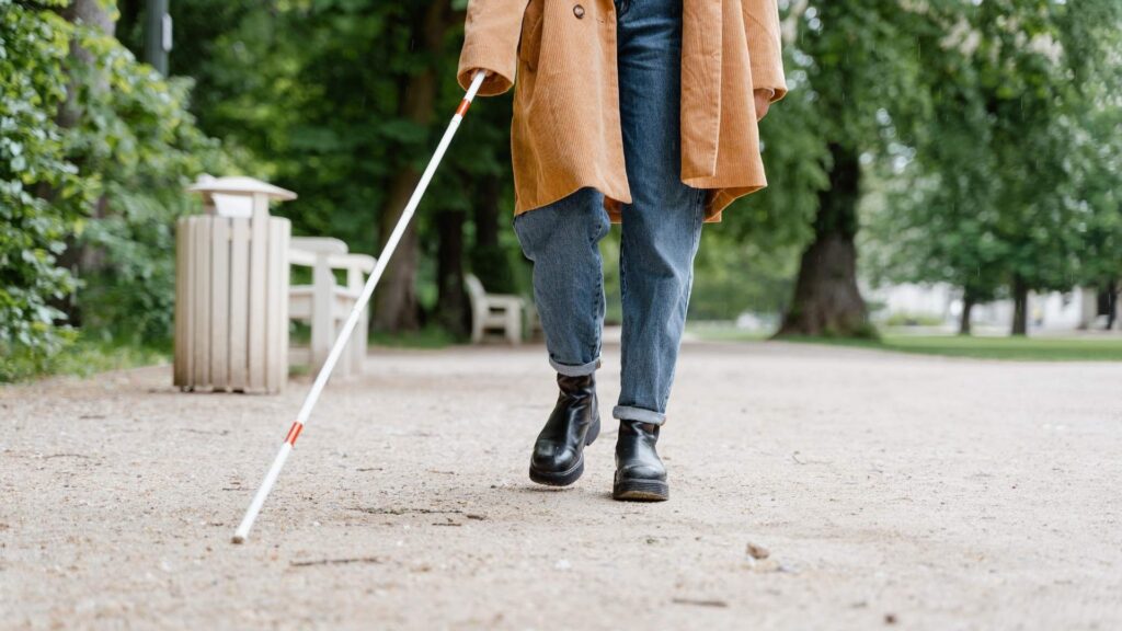 Person using a white cane while walking independently outdoors.