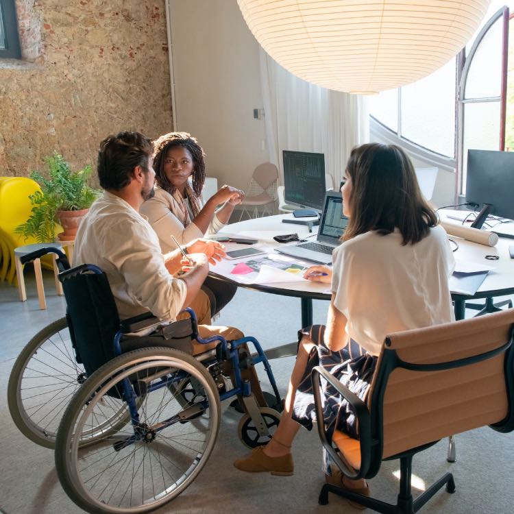 Inclusive workplace meeting with diverse professionals, including a wheelchair user collaborating with colleagues.