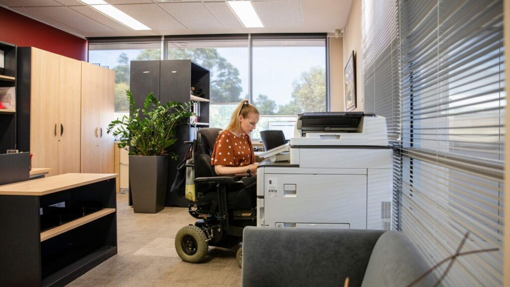 Wheelchair user working independently in an accessible office environment.