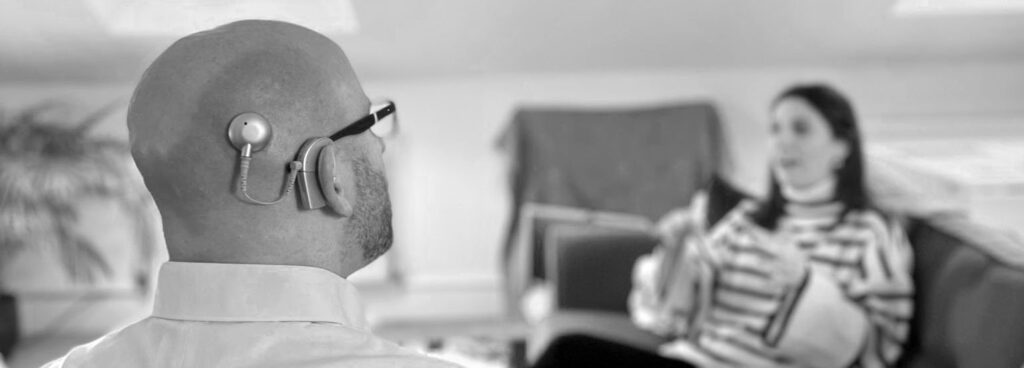 Person wearing a cochlear implant engaged in conversation during a meeting.