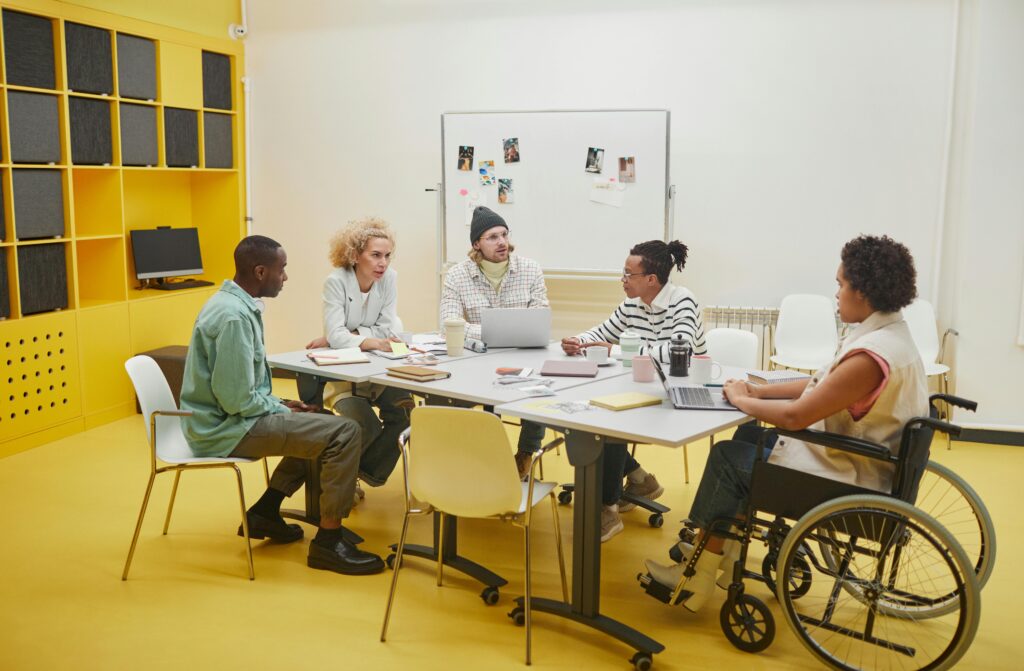 Diverse group of professionals in a collaborative meeting, including a wheelchair user in an inclusive workspace.