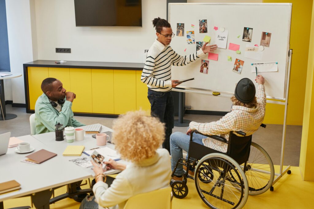 Team workshop and presentation in an inclusive workplace setting, including a wheelchair user participating in the discussion.
